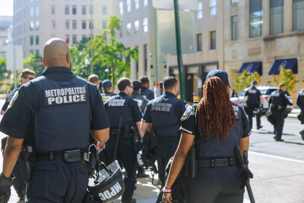 Group of Metropolitan Police officers walking down a city street, seen from behind, during daytime.
