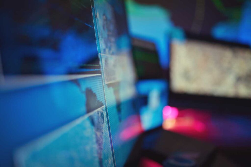 Close-up of computer monitors showing blurred maps, code, and data visualizations in a cybersecurity operations setting.