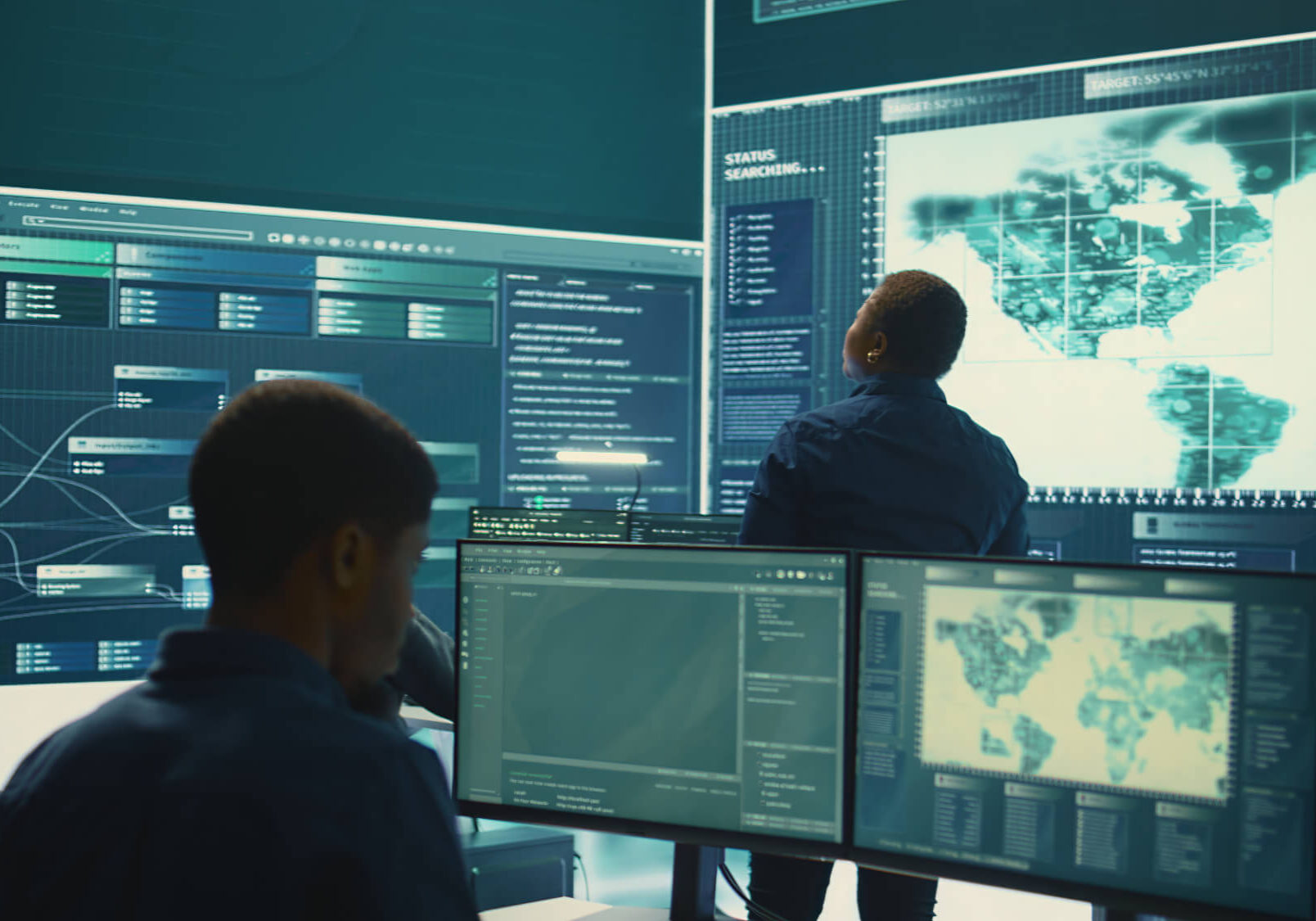 Three security professionals monitoring global data from multiple computer screens in a dark operations center.