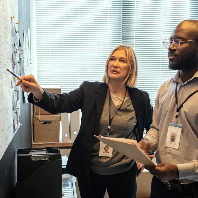 Two professionals discuss a case in an office, with one pointing at a detailed planning board.